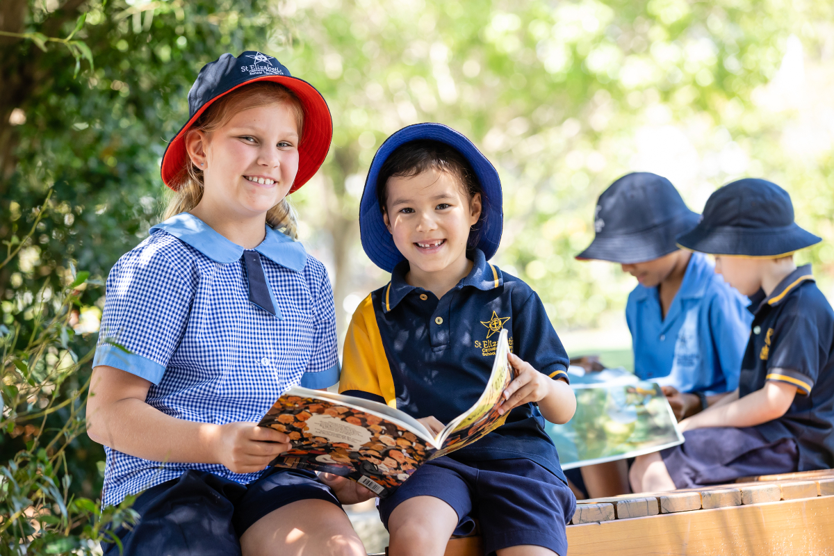 Two students sitting together outdoors reading books, highlighting literacy learning, friendship and enjoyment of reading in a relaxed school environment