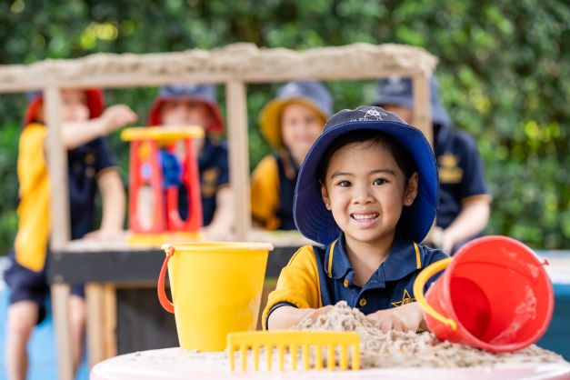 Young student playing with sand and buckets during an outdoor early years activity, highlighting sensory play creativity and learning through exploration
