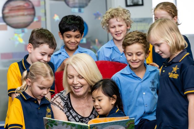 Teacher reading a picture book to a small group of students, highlighting shared literacy learning, engagement with reading and a nurturing classroom environment